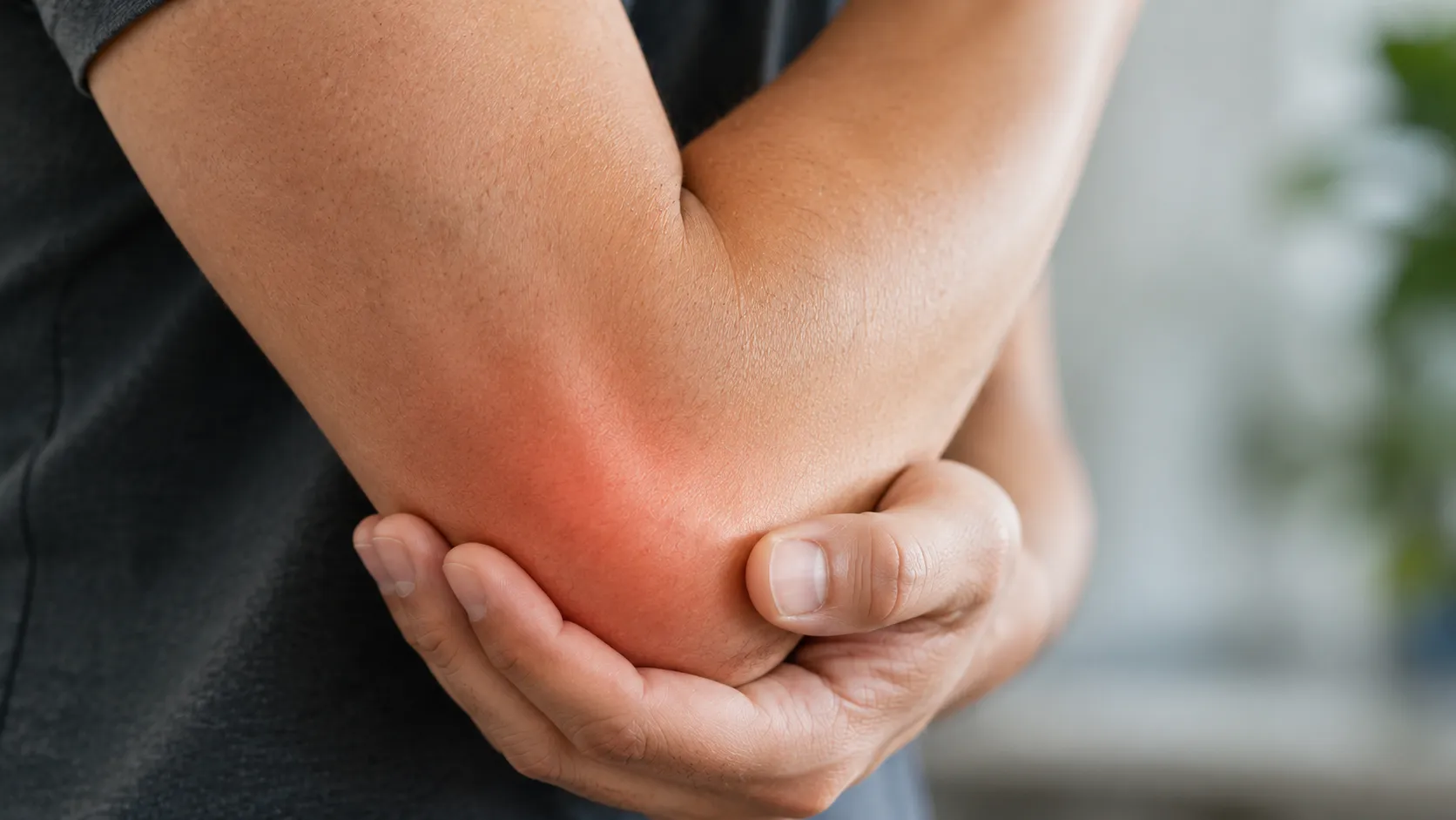 A close-up view of a person holding their elbow, with a red digital glow indicating pain or discomfort at the joint.
