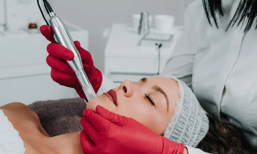 Provider in red gloves performing Microneedling Denville, NJ on a woman with eyes closed.